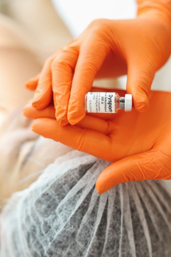 services-02 Orange-gloved hands holding a small Dysport vial in a healthcare setting.