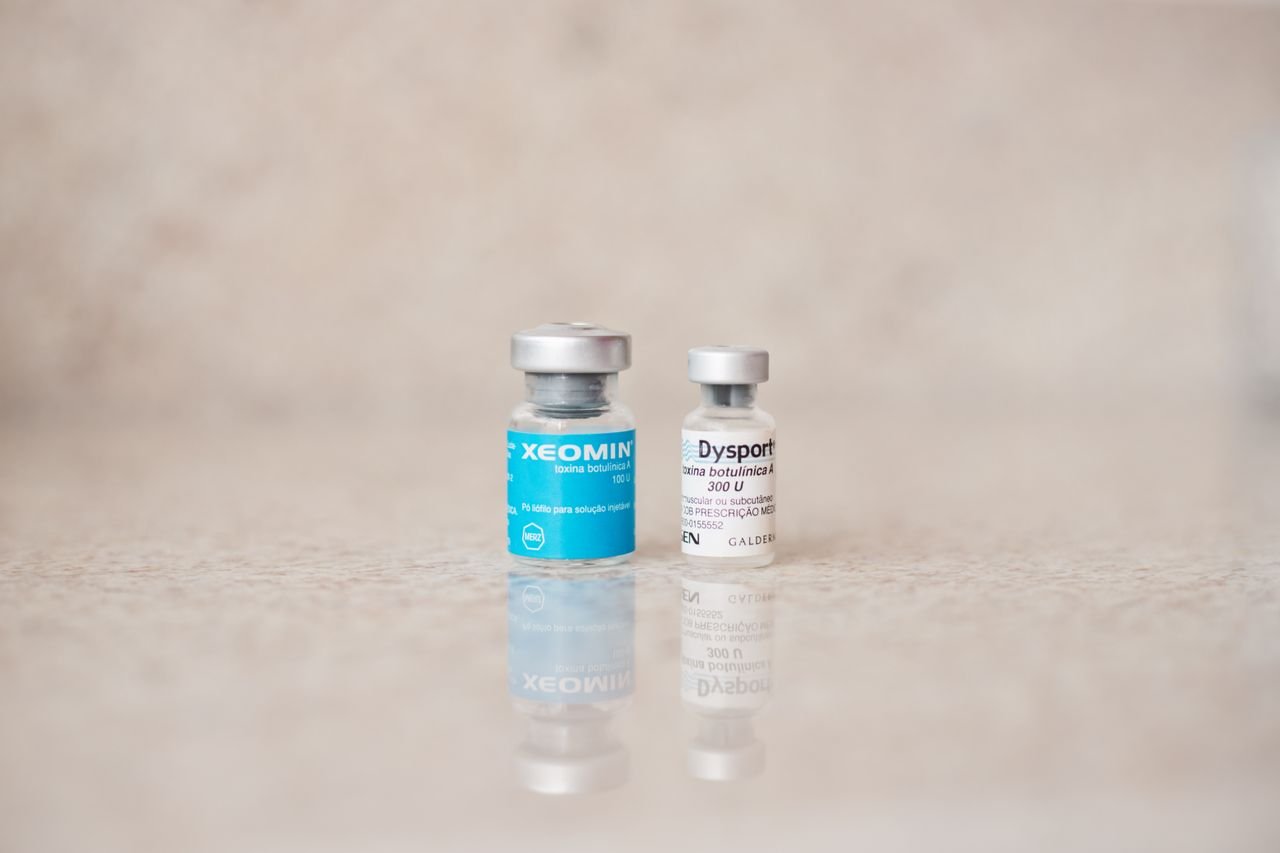 our-story Close-up of Xeomin and Dysport bottles reflecting on a surface, shot indoors.
